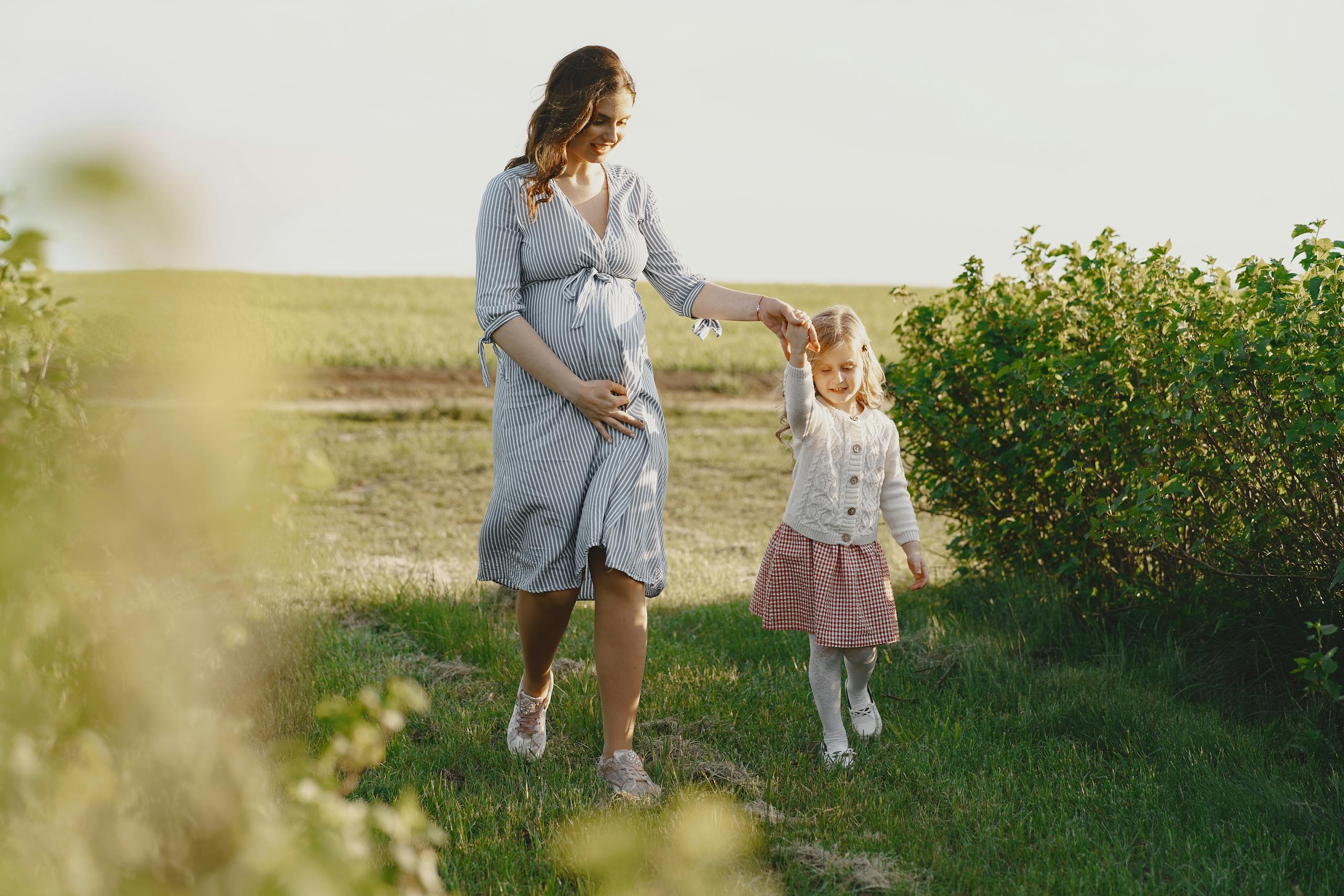 A pregnant mother enjoying a summer walk with her daughter in a green field.