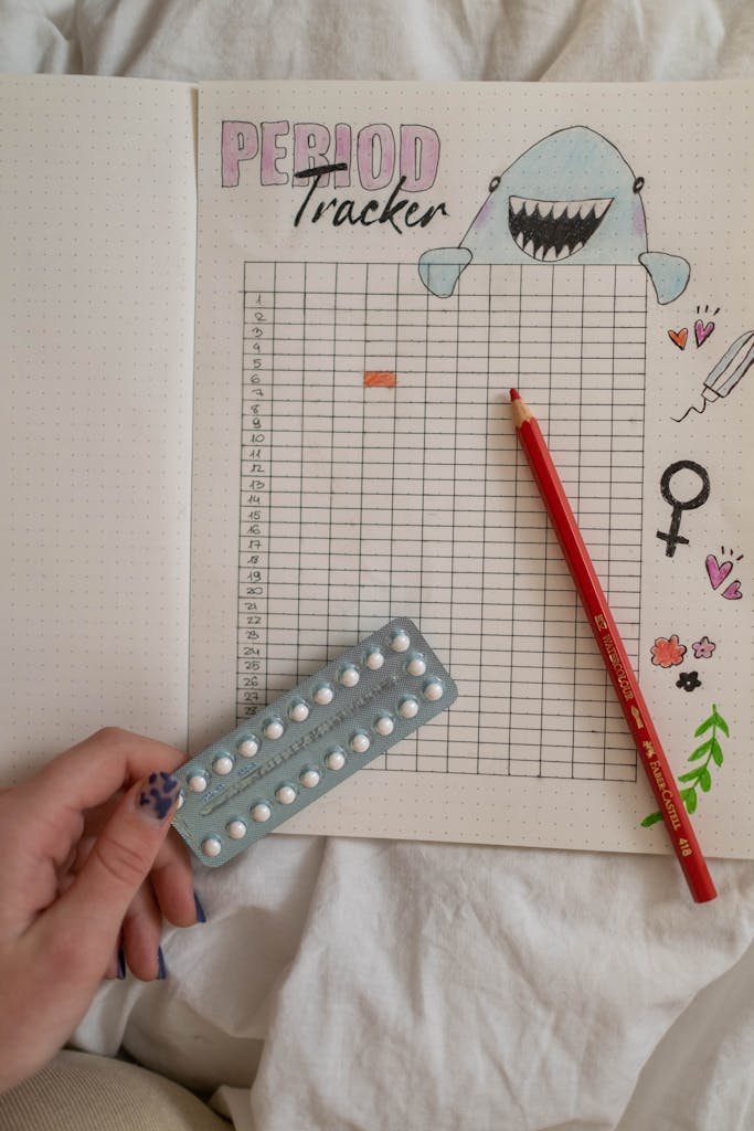 Creative period tracker notebook with a hand holding birth control pills.